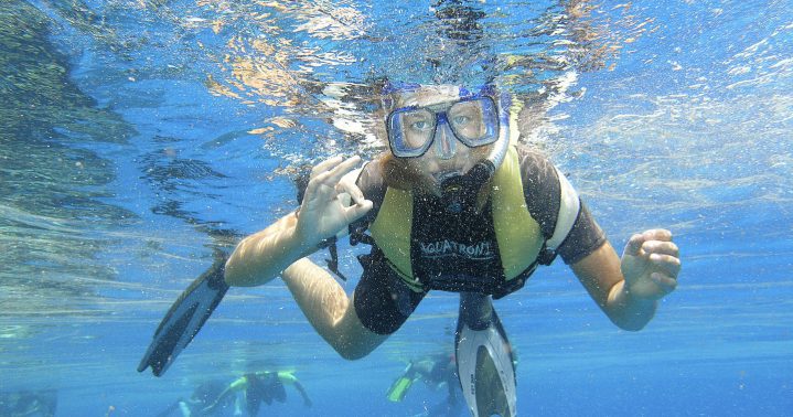 Frau mit Schnorchel unter Wasser, die das handzeichen für 