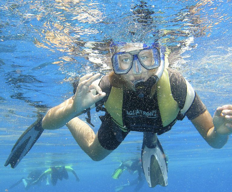 Frau mit Schnorchel unter Wasser, die das handzeichen für 