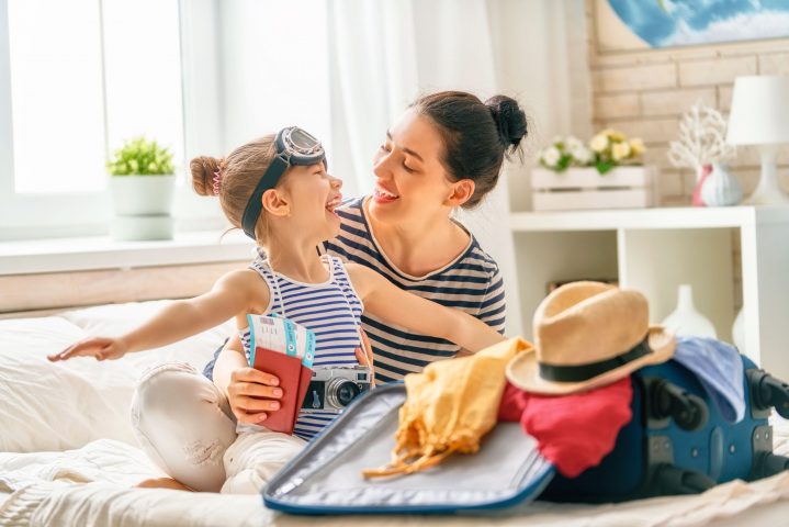 Mutter und kleines Kind sitzen vor einem geöffneten Reisekoffer und haben Spaß