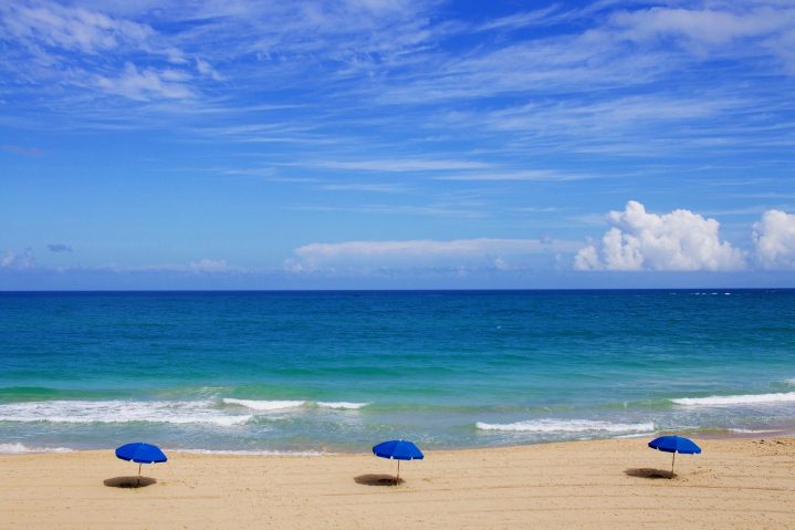 Ein einsamer Strand mit blauen Sonnenschirmen.