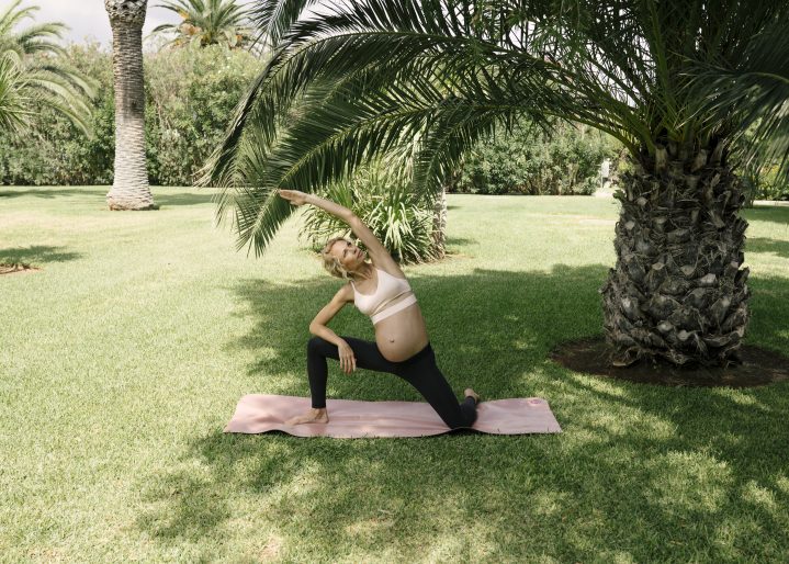 Schwangere Frau macht Side Angel Übung auf der Wiese unter Palmen