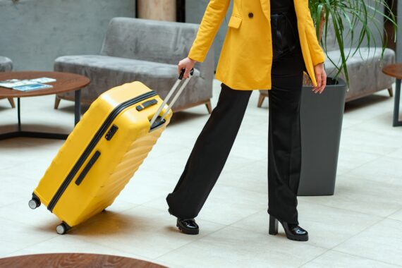 Eine Frau mit gelbem Mantel und gelbem Koffer zieht ihren Koffer durch ein Hotel