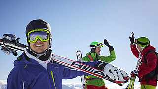 Menschen in warmer Kleidung tragen ihre Skier und lachen