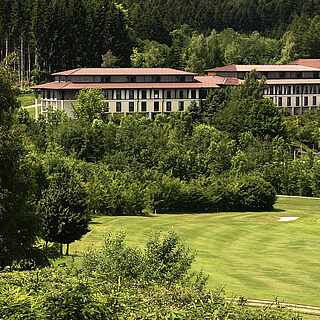 Grüne Wiese, auf der ein Ball liegt; im Hintegrund ein Golfplatz