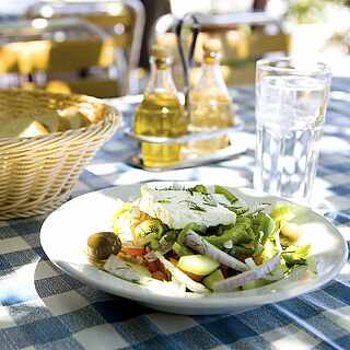 Gedeckter Tisch mit Vorspeisensalat, Olivenöl und Brotkorb auf weißblau-karierter Tischdecke