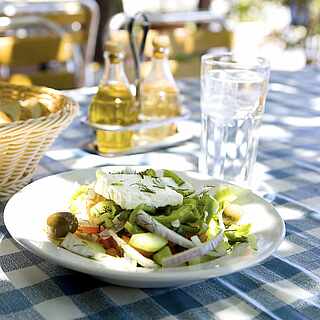Gedeckter Tisch mit Vorspeisensalat, Brotkorb und Olivenöl auf weiß-blau-karierter Tischdecke