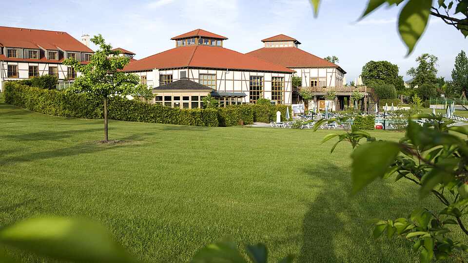 Grüne Wiese mit Bäumen vor dem ROBINSON Club Fleesensee, Gebäude im Hintergrund