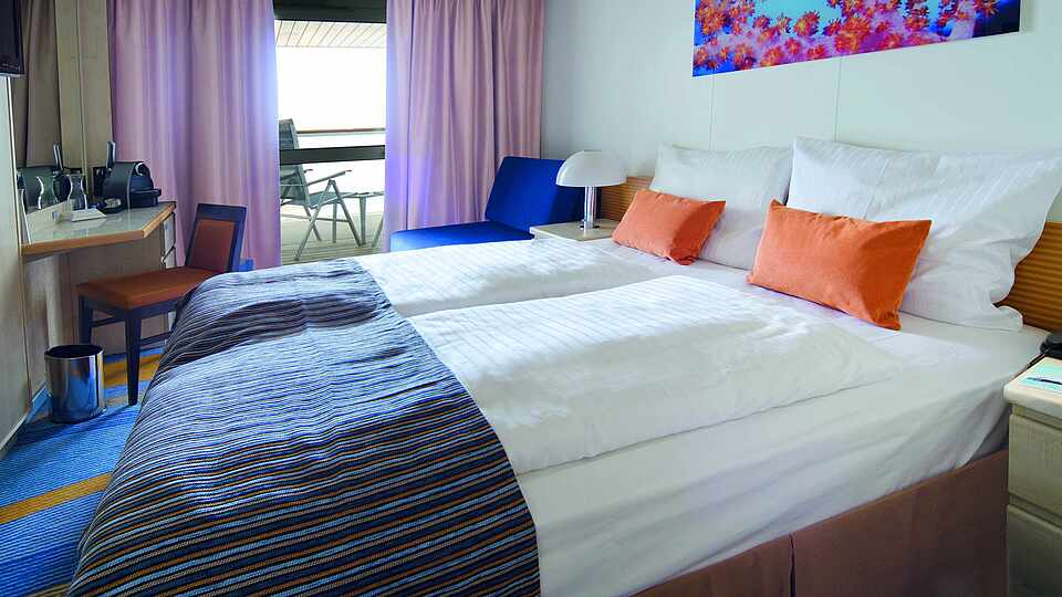 Eine Kabine auf der Mein Schiff 2 mit Doppelbett und Blick über den Balkon nach außen