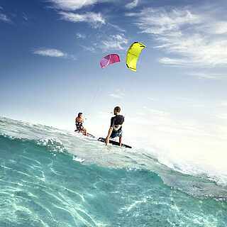 Zwei Menschen kiten auf türkis-blauem Meer