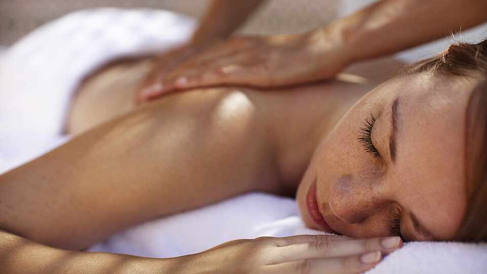 Frau mit geschlossenen Augen erhält eine Rückenmassage