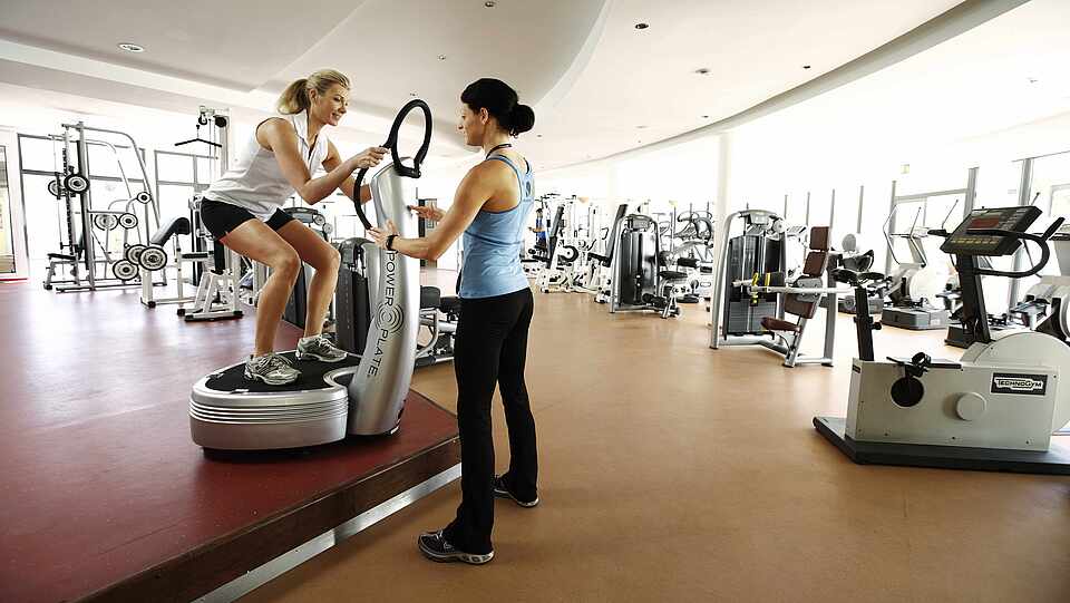 Frau mit Personal Trainer beim Vibrationstraining Power Plate