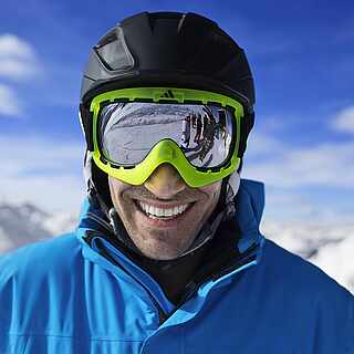 Mann mit Skibrille und Helm mit weißen Bergen im Hintergrund