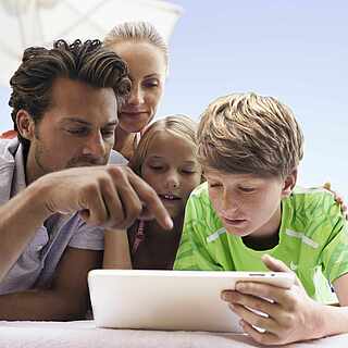 Vatrer, Mutter, Sohn und Tochter schauen zusammen interessiert auf ein Tablet 