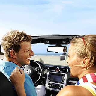Ein Üärchen sitzt lachend im Cabriolet von TUI Cars. 