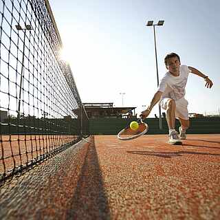 Ein Mann erreicht knapp einen Tennisball und schlägt ihn über das Netz