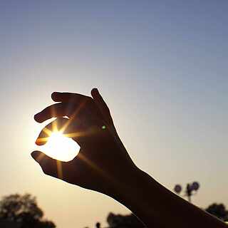 Hand formt mit den Fingern einen Kreis, welcher die Konturen der Sonne umramt