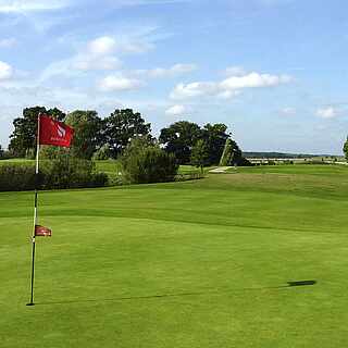 Gepflegter Golfplatz unter blauem Himmel mit roter Fahne im Vordergrund