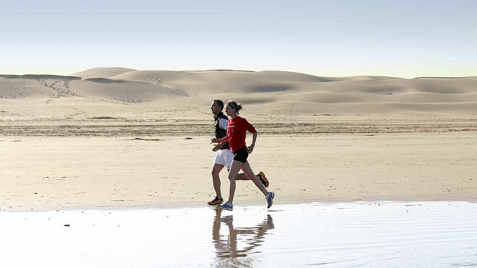 Zwei Menschen laufen am Strand in Marokko