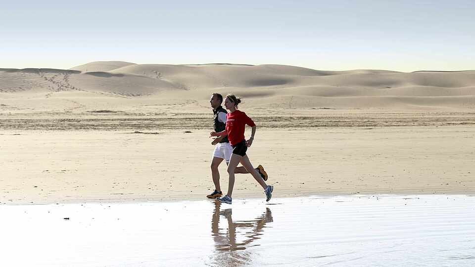 Zwei Menschen laufen am Strand in Marokko