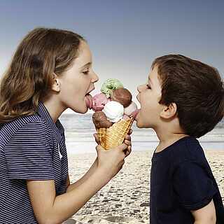 Zwei Kinder schlecken ein großes Eis am Strand