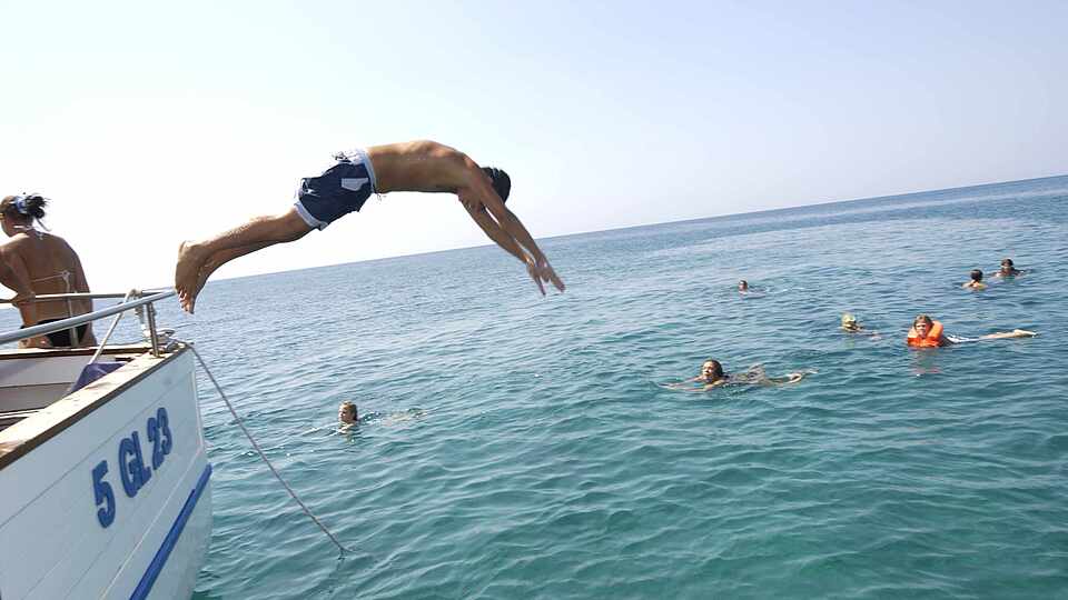 Mann springt von einem Boot in das blaue Meer