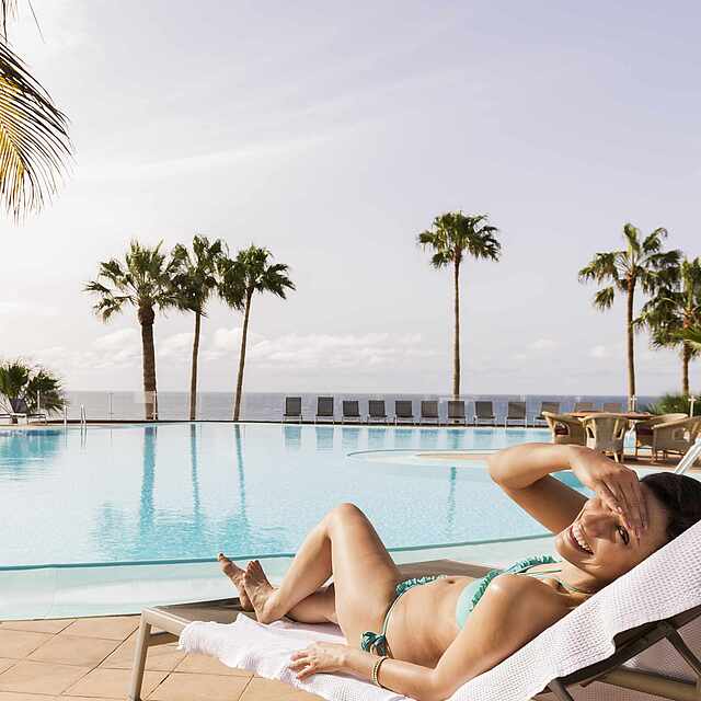 Großer Outdoorpool im WellFit-Bereich Frau liegt auf einer Liege am Outdoorpool und sonnt sich