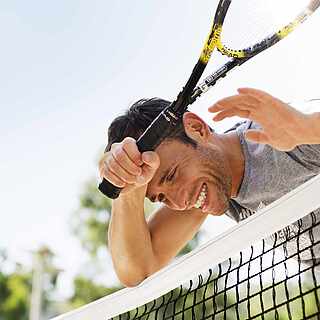 Mann lehnt sich mit einem Tennisschläger auf ein Tennisnetz