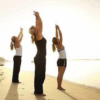 Drei Frauen machen Übungen am Strand an der Wasserkante.