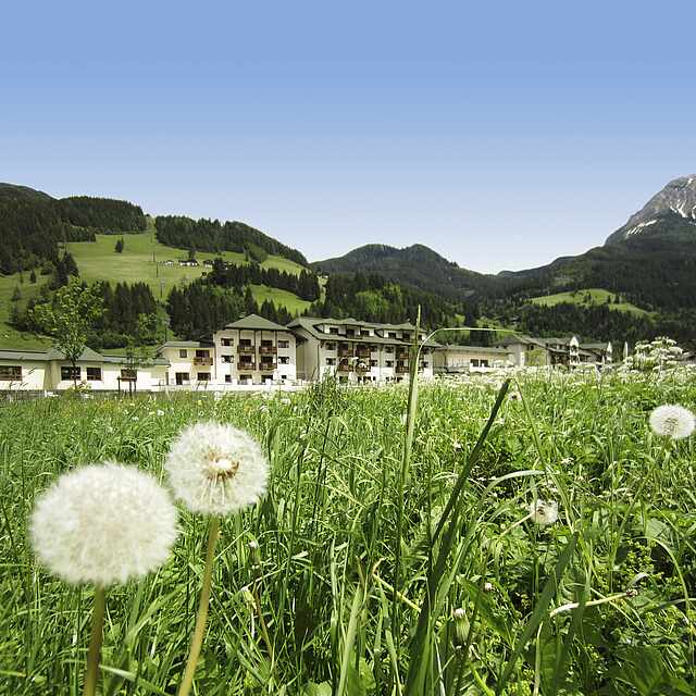 Aussicht auf die Berge im ROBINSON Club Amade Grünfläche mit Hotelanlage und Bergen vor blauem Himmel