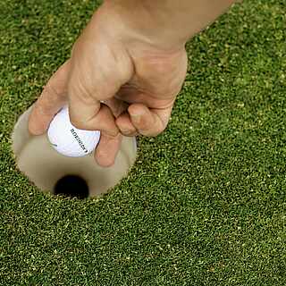Eine Hand greift Golfball aus einem Golfloch