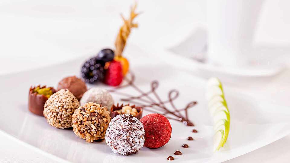 Verschiedene Pralinen sind mit Beeren und Schokoladen-Creme auf einer Platte angerichtet