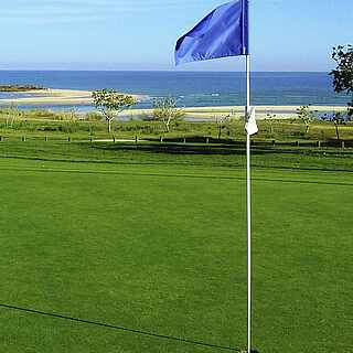 Golfplatz mit Ausblick aufs Meer und blauer Fahne