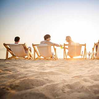 Gruppe junger Pärchen sitzt am Strand auf Liegestühlen und unterhält sich