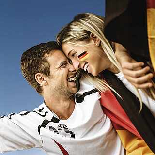 Ein Pärchen das sich umarmt und beim Fußball Deutschland anfeuert