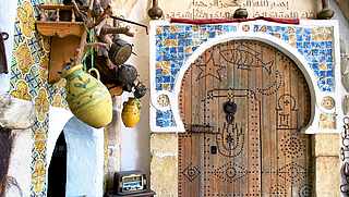 Orientalisch verzierte Holztür mit Rundbogen und bunten Tonkrügen an der Wand